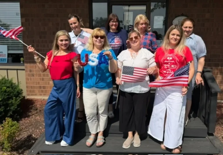 Caregiving team with American flags and USA balloon letters on the steps of the European Service office in Lombard, Illinois.