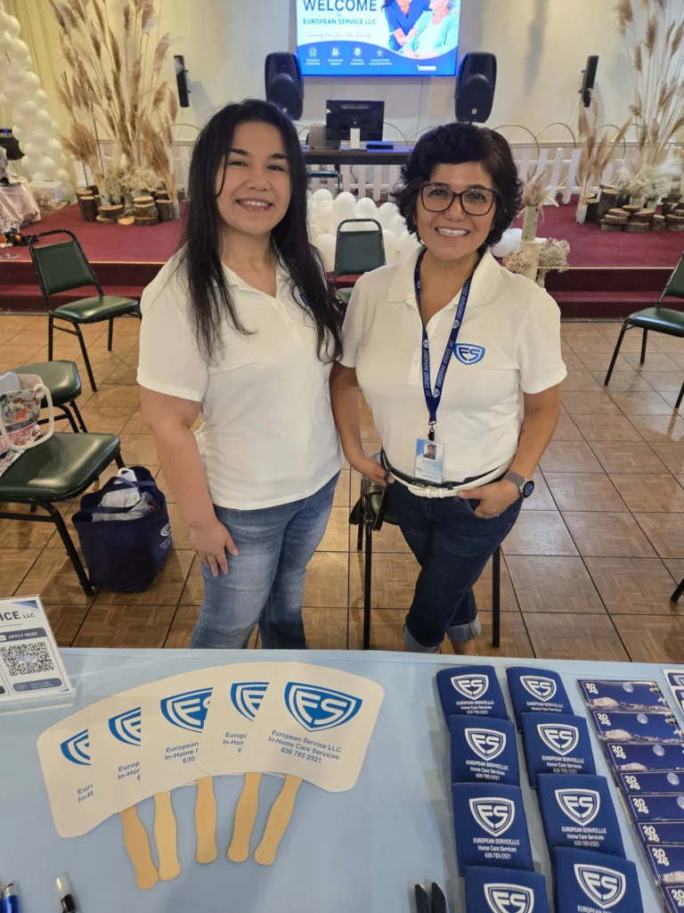 Two European Service team members in branded polo shirts at the agency’s information table during a senior community event.