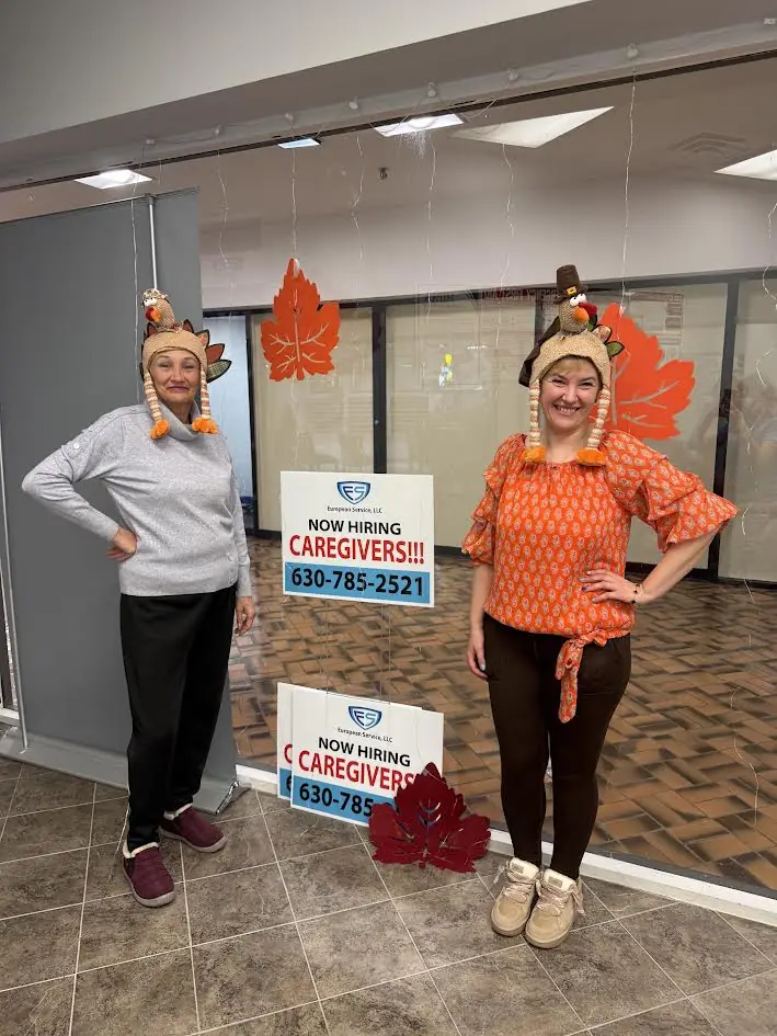 Two team members in turkey hats beside “Now Hiring Caregivers” signs at the European Service office entrance in Niles, Illinois.